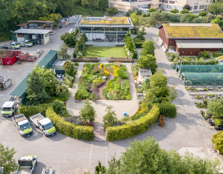 Vogelperspektive von Betriebsgelände mit Gebäude, Halle, Schaugarten, Lagerplatz und Fahrzeuge